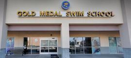 Exterior view of Gold Medal Swim School showing the entrance doors and large gold letters spelling the school's name above the entrance.